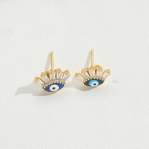 Detail of gold evil eye stud earrings with blue enamel center and clear zircon accents
