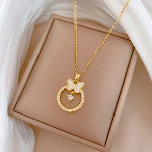 Detail of a gold butterfly pendant with white shell and zircons on a beige jewelry box