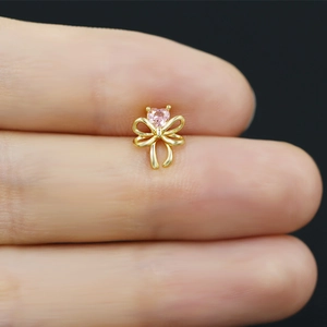 Macro shot of tiny gold bow stud earring with a pink heart zircon held between fingers