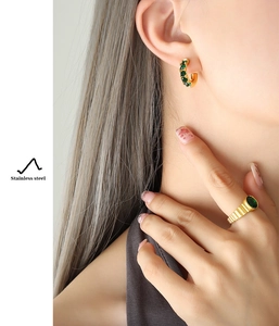 Détail des boucles d'oreilles en forme de C en acier doré 18K avec zircons verts