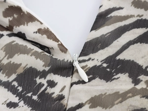 Detail of a white zipper closure on a beige chiffon dress with black tiger print pattern