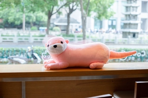 Pink plush otter doll lying on a wooden counter in soft natural light close-up