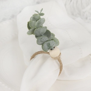 Close-up of eucalyptus napkin ring with wood bead and twine on white linen napkin