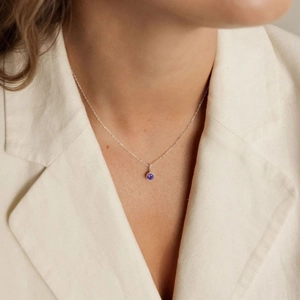 Close-up of a minimalist silver chain necklace with a small round purple gemstone pendant