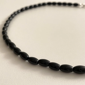 Close-up of polished black onyx oval beads on a minimalist necklace with reflective finish