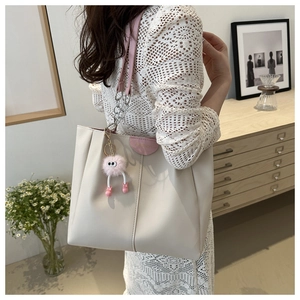 Dettaglio borsa tote crema con accenti rosa, logo fashion e ciondolo di peluche su catena