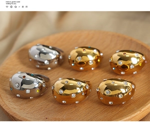 Close-up of gold and silver teardrop dome rings with colorful rhinestone inlay on a wooden tray