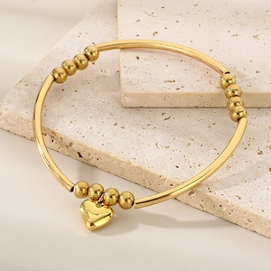 Détail d'un bracelet à billes dorées avec pendentif cœur sur fond de pierre naturelle