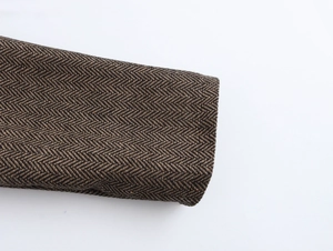 Détail de la texture en tweed à chevrons marron sur la manchette d'une veste