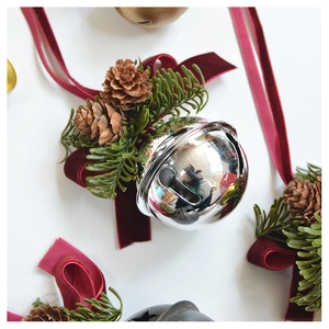Close-up of a silver Christmas bell with pine cones, needles, and a red velvet bow