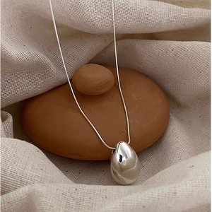 Macro detail of polished silver teardrop pendant on sleek snake chain over natural stones
