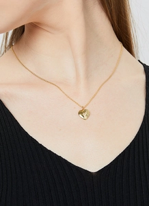 Detailed close-up of a golden heart necklace with feather texture on a female model
