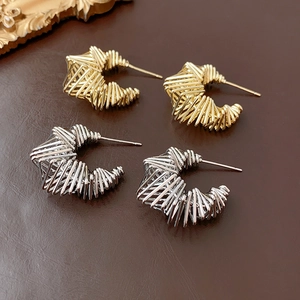 Detailed shot of twisted C-shaped gold and silver earrings on brown leather background