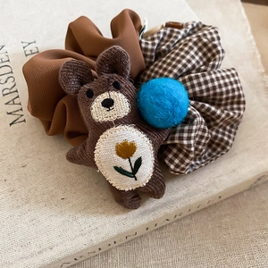 Close-up of brown plaid fabric scrunchie with cute bear plush and blue pom-pom detail