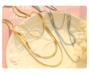 Detail of layered gold and silver flat snake chains on vintage ceramic plate