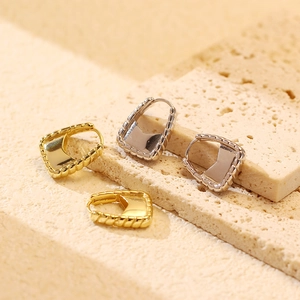 Macro shot of silver and gold ribbed hoop earrings with shield detail on stone surface