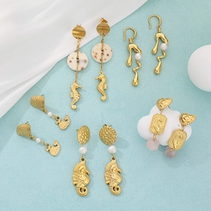 Macro shot of gold ocean-themed earrings featuring seahorse, shells, pearls, and natural stones