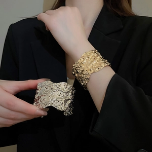Detail of gold and silver textured irregular metal open cuff bracelets on a model