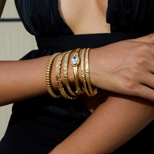 Dettaglio di bracciali dorati a strati con texture martellata e pietra di zircone
