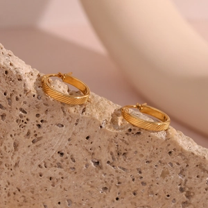 Macro detail of gold hoop earrings with diagonal stripe texture on minimalist stone base