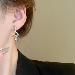 Close-up of curved silver snake earrings with zircon stones worn on the ear
