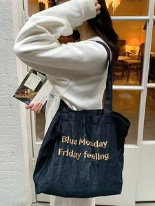 Fashionable black denim tote bag with gold embroidery shown in a lifestyle model shot