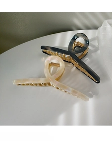Detail of cream white and marble grey hair claws with gold metal teeth on white surface