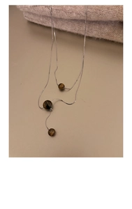 Detail einer silbernen Doppelkette mit braunen Tigerauge-Perlen auf Strickstoff