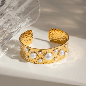 Hammered gold stainless steel open cuff bracelet with white faux pearls on stone surface