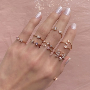 Adjustable 18K rose gold rings with butterfly and flower motifs on a pink background