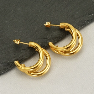 Macro shot of gold-plated multi-layer geometric hoop earrings on slate and beige fabric