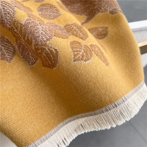 Detail of yellow knitted scarf with brown leaf pattern and decorative fringe texture