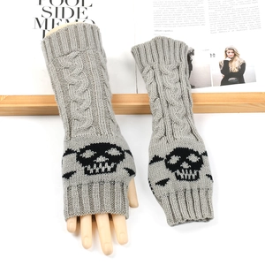 Detail of grey knitted arm warmer with black skull pattern on a wooden stand