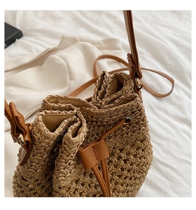 Detail showing woven paper straw texture and brown PU leather drawstring on bucket bag