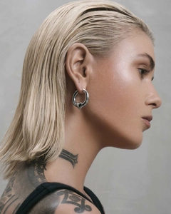 Close-up of polished silver hoop earring with a black 3D heart charm on a female model