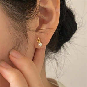 Detailed shot of golden bunny ears earrings with white lustrous pearls worn by a model