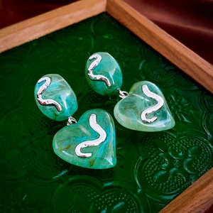 Macro detail of green marble texture acrylic heart earrings with silver S-curve relief