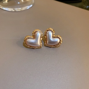 Close-up of heart-shaped earrings with gold textured edges and pearl white centers