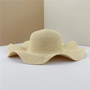 Detail of a beige wide-brim straw hat with wavy edges and fine woven texture