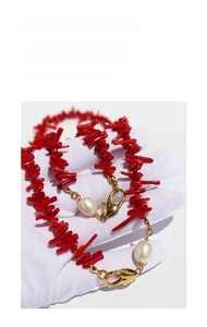 Detail of red branch coral necklace with white pearls and gold clasp held by a hand