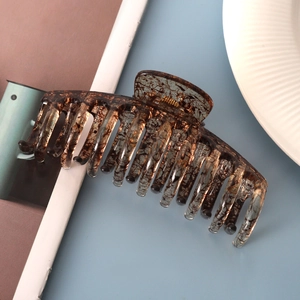 Macro detail of a transparent amber hair claw clip with stylish brown ink splatter pattern