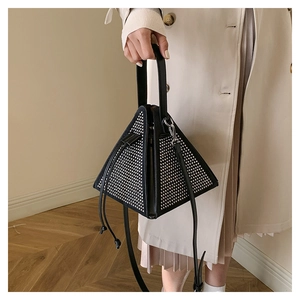 Detail of a black pyramid bag with silver studs carried by a model in a beige coat