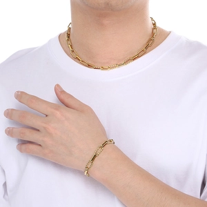 Detail of gold paperclip chain necklace and bracelet set worn by male model on white tee