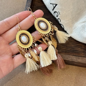 Detail of bohemian long tassel earrings with golden leaf charms and yellow enamel