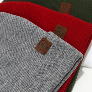 Three rib-knit beanie hats in grey, red, and green with square leather logo patches