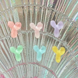 Close-up of colorful Y-shaped resin hair clips in pastel tones on a shell background