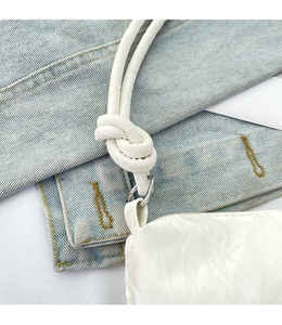 Detail of white drawstring bag featuring knot shoulder strap and metallic ring hardware