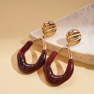 Detail of amber resin drop earrings with gold metal studs on a minimalist stone surface