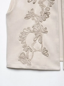Detailed macro of beige faux suede vest featuring intricate vine embroidery and floral textures