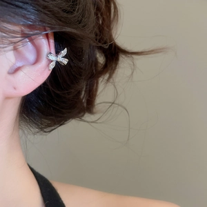 Macro shot of a silver bow-shaped ear cuff with sparkling zircons worn on the ear